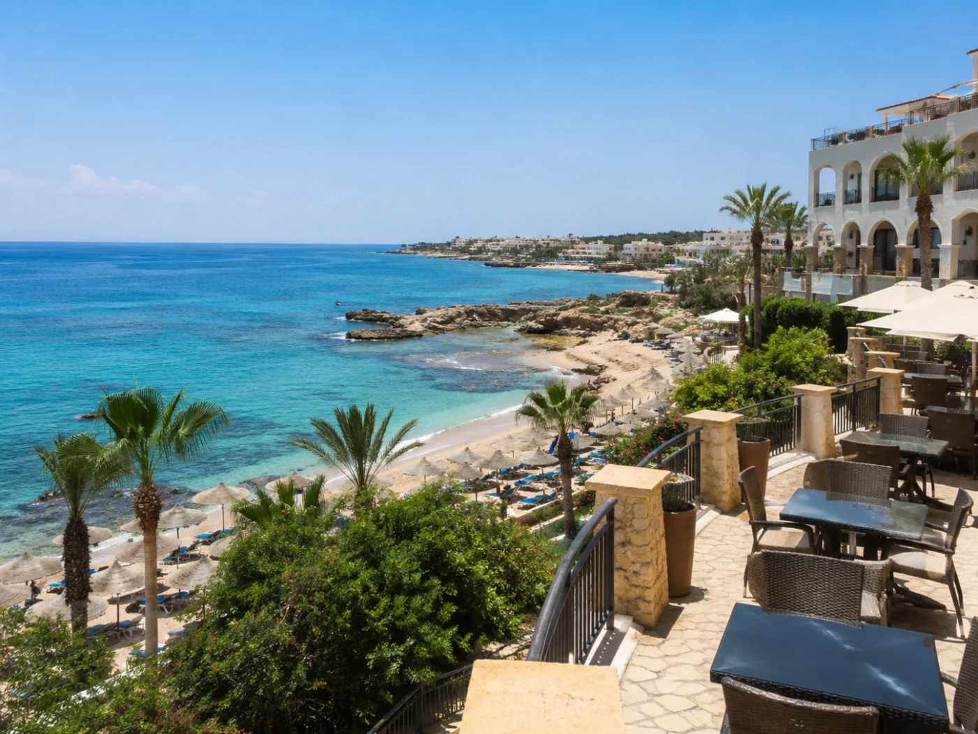 Strand aan de kust van Cyprus met strodaken-parasols, turquoise zee en een terras met tafels