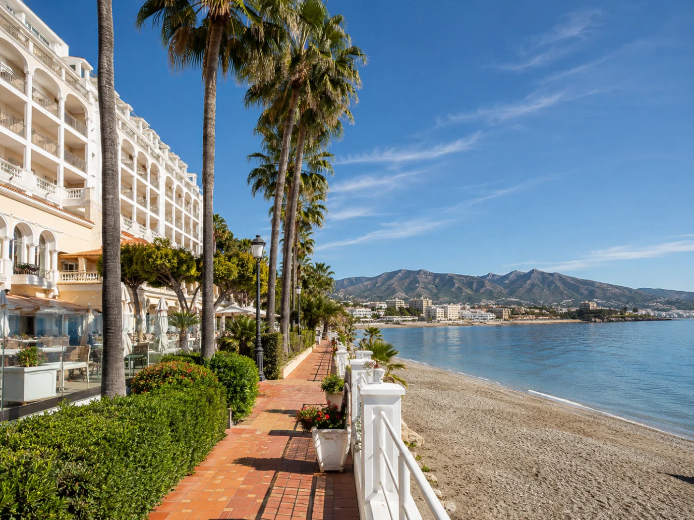 Spring in March on the Southern European coast: palm trees along a boulevard with beach, sea, and mountains in the background
