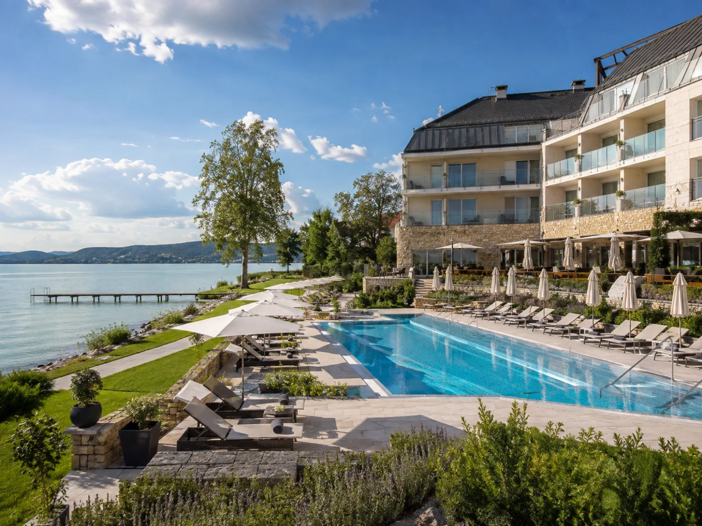 Elegant wellnesshotel aan het Balatonmeer in Hongarije met buitenzwembad, parasols, ligbedden en een steiger in het meer