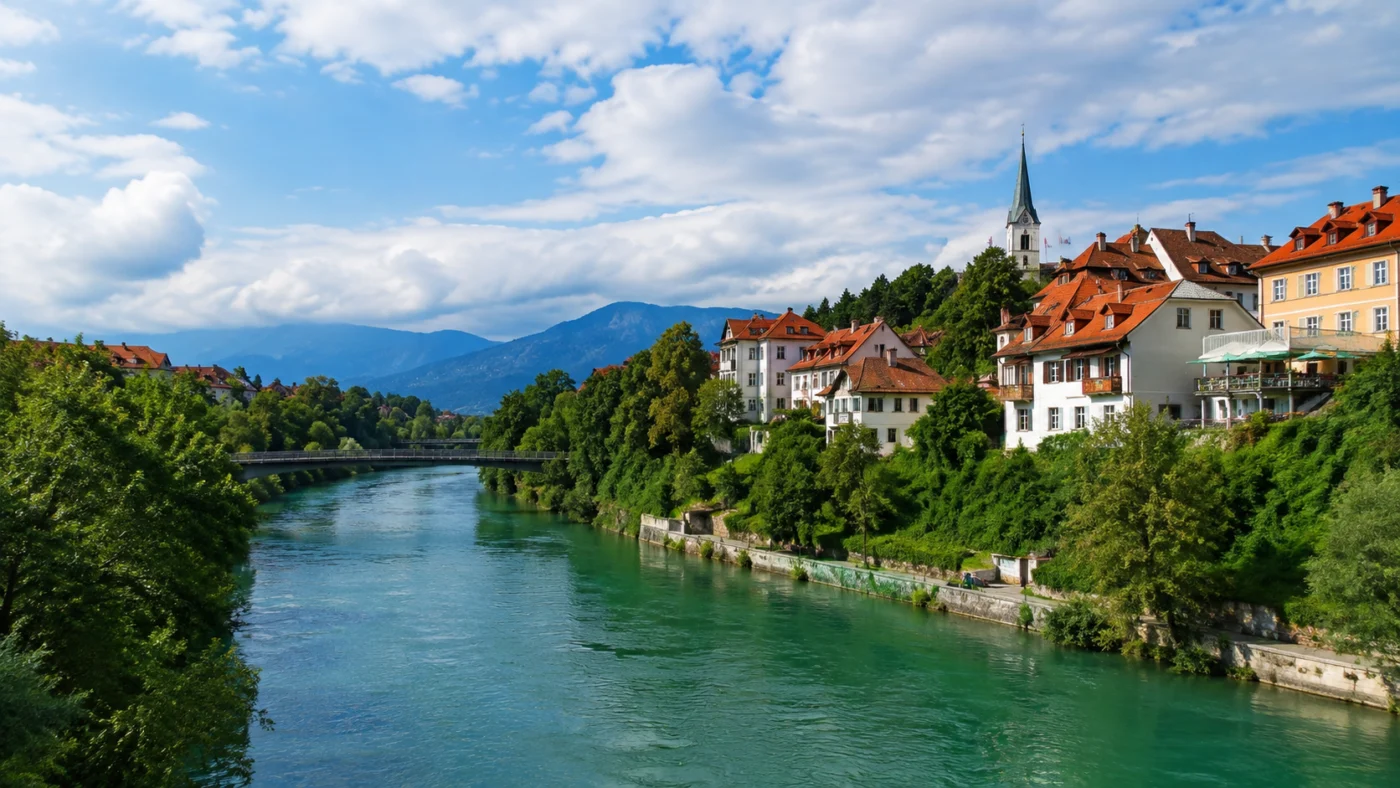 Sloveens stadje met rode daken en een kerktoren aan een turquoisegroene rivier, met beboste oevers en bergen op de achtergrond