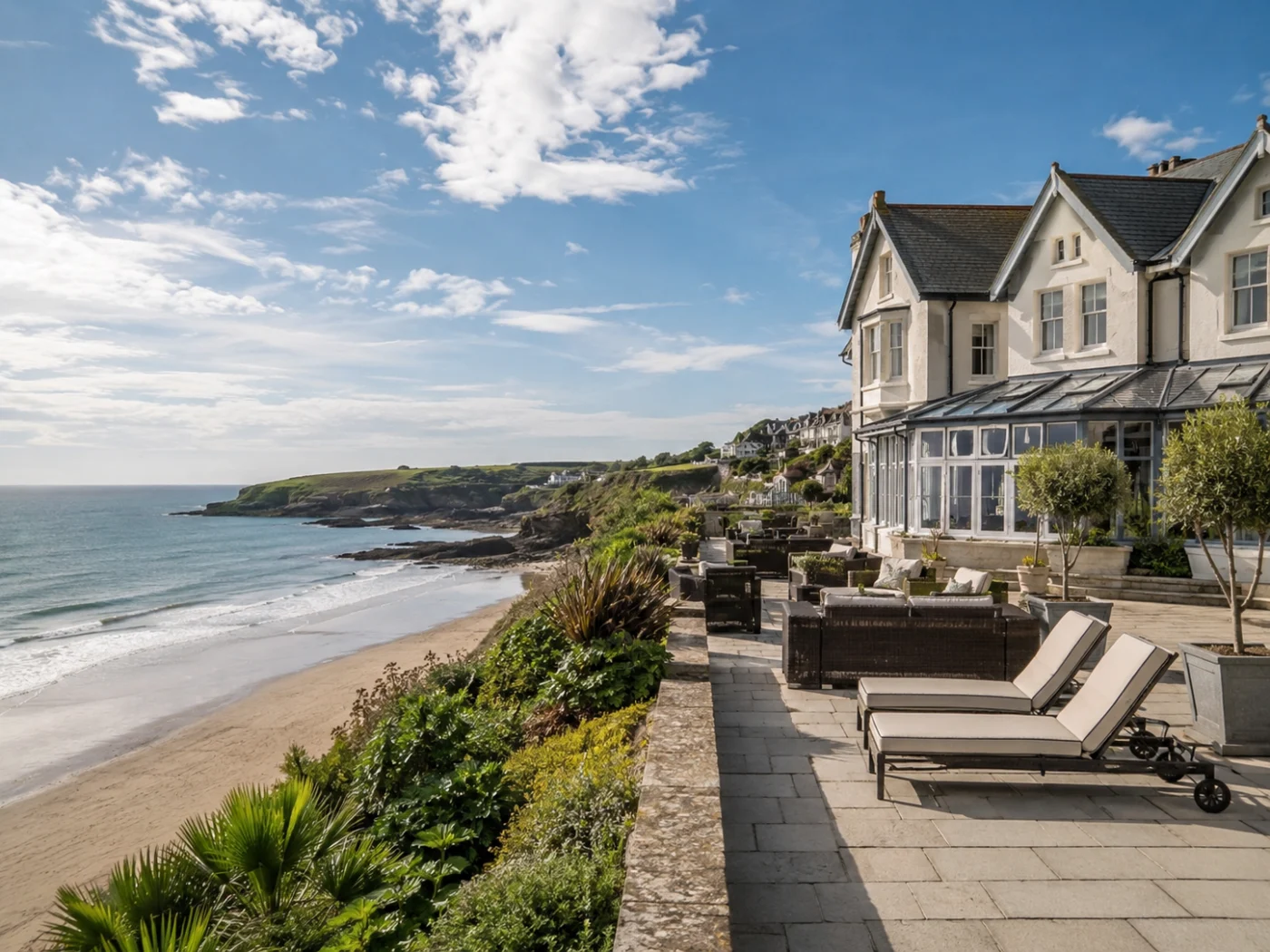 Klassiek Brits kusthotel met terras en ligbedden boven het strand en de kliffen van Cornwall